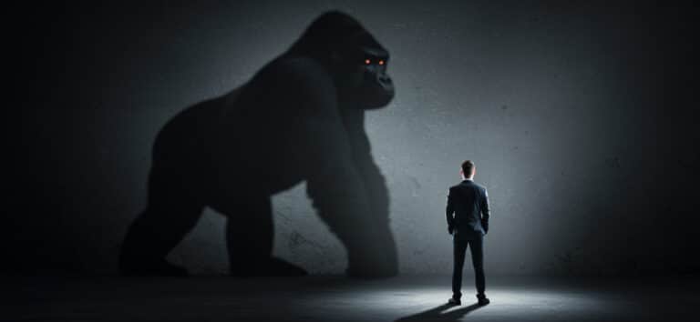 Small business founder standing in front of large gorilla shadow symbolizing intimidating market leaders
